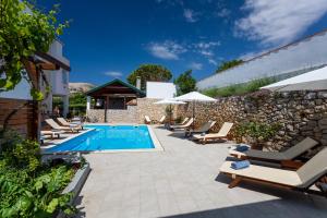 a pool with lounge chairs and a stone wall at Apartments Maja and Sanja in Baška