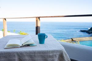 a book and a cup on a table with the ocean at Gardenvilla Shirahama in Shimoda