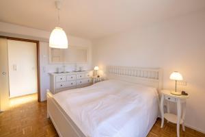 ein weißes Schlafzimmer mit einem großen weißen Bett und zwei Tischen in der Unterkunft Ferienwohnung Seeblick mit Blick auf die Alpen in Wasserburg