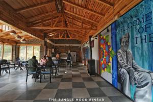 a dining room with people sitting at tables and a mural at The Jungle Hook Binsar in Almora