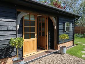 a black shed with a wooden door and two potted trees at The Forge in Stowmarket