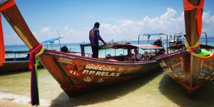 a wooden boat on the beach with people on it at Phi Phi Relax Beach Resort in Phi Phi Islands
