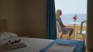 a woman sitting in a chair looking out the window at the ocean at Phoenix-Hotel in Plakias