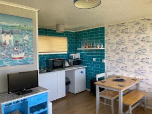 a kitchen with blue tiled walls and a table with a television at Chalet 65 in Chapel Saint Leonards