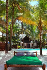a bed on the beach with palm trees and a pool at Zanzibar Gem Beach Bungalows in Bwejuu
