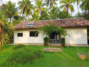 a small white house with palm trees in the background at Coconut Garden River Villa in Galle