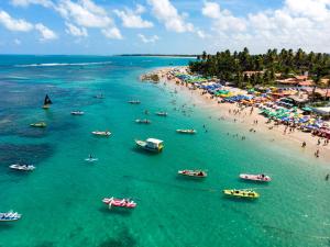 a beach with people and boats in the water at Cupe Beach Living - Porto de Galinhas in Porto De Galinhas