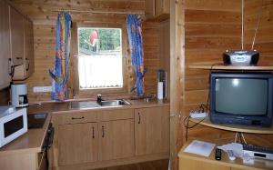 una cocina con TV y un lavabo en una cabaña de madera en Ferienhaus Nr 25, Typ A, Feriendorf Jägerpark, Bayerischer Wald, en Viechtach