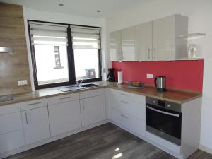 a kitchen with white cabinets and a red wall at Ferienhaus Leo in Blankenrath