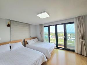a bedroom with two beds and a large window at Hera Castle Pension in Seogwipo