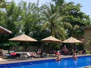 a group of people sitting around a swimming pool with umbrellas at Handagedara Resort & Spa in Mirissa