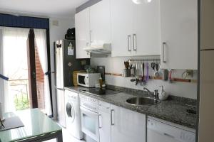 eine weiße Küche mit einer Spüle und einer Mikrowelle in der Unterkunft La Tilar, apartamento con gran terraza a 3 km de la playa in Llanes
