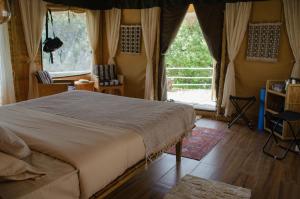 a bedroom with a bed and a large window at DugDug Camps - Glamping Amidst Nature in Bhīm Tāl