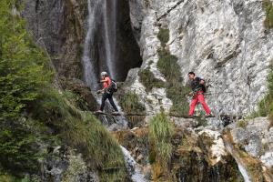 tres personas cruzando un puente de cuerda frente a una cascada en Albergo Genzianella, en Fiavè