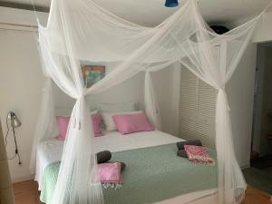 1 dormitorio con cama con dosel y almohadas rosas en Villa 13, Coral Estate, en Willibrordus