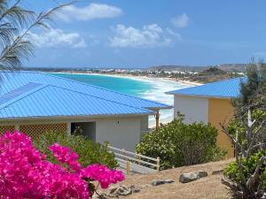 a house with a blue roof and a beach with pink flowers at Studio Orient Bay in Orient Bay