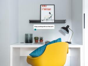 a desk with a yellow chair and a table with a poster at numa I Munico Apartments in Munich