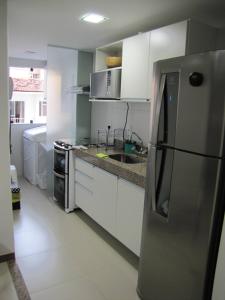 cocina con armarios blancos y nevera de acero inoxidable en Moderno apartamento perto da praia, en Maceió