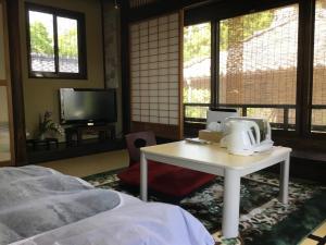 a bedroom with a table and a tv and windows at Minshuku Hiroshimaya in Kumamoto