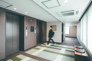 a person walking down a hallway in an office building at Hotel Kuretakeso Takayama Ekimae in Takayama