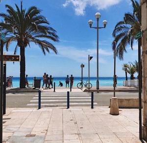 a beach with palm trees and people walking on the beach at Studio Magenta in Nice