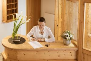 una mujer sentada en una mesa escribiendo en un papel en Garni-Hotel mir.es, en Tirolo