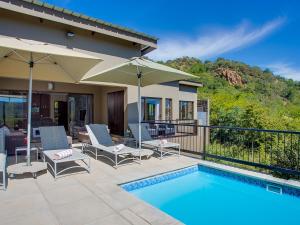 a pool with chairs and umbrellas next to a house at Shepherds Tree Game Reserve in Pilanesberg