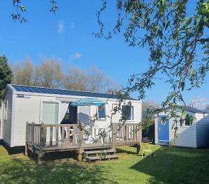 a mobile home with a deck and an umbrella at Camping Caravaning Les Cerisiers Berck sur mer in Verton