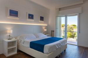 a white bedroom with a large bed and a window at Hotel Tarabella in Forte dei Marmi