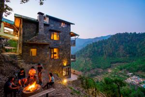 a group of people standing around a fire pit in front of a house at Zostel Homes Ramgarh, Nainital in Rāmgarh