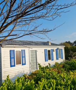 uma casa branca com persianas azuis e arbustos em La belle Perrochoise 13 mobilhome em La Cotinière