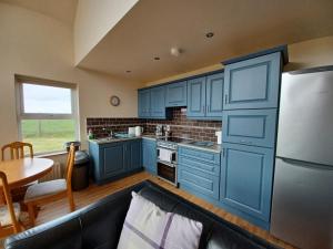 a kitchen with blue cabinets and a table and a refrigerator at The Chalet at Corvally in Portrush