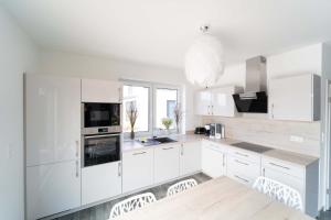 a white kitchen with white cabinets and a table and chairs at Ferienhaus Seewind am Harkebrügger See mit Sauna und Kamin in Barßel