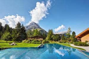 a swimming pool in a garden with a mountain in the background at Post Lech Arlberg in Lech am Arlberg