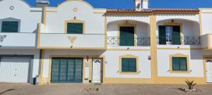 a large white building with green shuttered windows at Vivenda Faria in Vila Nova de Milfontes