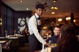 a man standing at a table with a vase in a restaurant at Van der Valk Zaltbommel-A2 in Zaltbommel