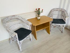 2 sillas de mimbre y una mesa de madera con un jarrón de flores en Villa Horyzont, en Międzywodzie
