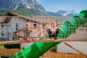 three children are sitting in a cage on a water slide at Hotel Tirolerhof - Familotel Zugspitze in Ehrwald