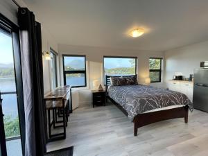 a bedroom with a bed and a desk and windows at Private Oceanfront Room With Hot Tub & Firepit - Shore Thing in Ucluelet