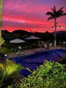 a sunset over a swimming pool with umbrellas at Magnífica casa de campo, próxima a São Paulo!! in Santana de Parnaíba