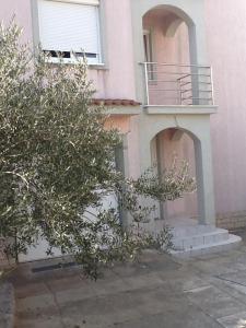 um edifício cor-de-rosa com uma varanda e árvores em frente em Apartment and Rooms Santini em Sveti Filip i Jakov