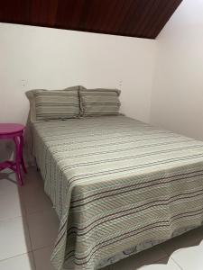 a bed with a striped blanket and a pink stool at Chalé Serrano in Bananeiras