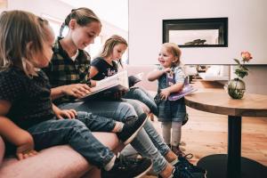 een vrouw die een boek leest voor drie meisjes in een woonkamer bij Kinderhotel Stegerhof in Donnersbachwald