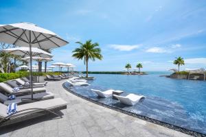 a pool with chairs and umbrellas next to the ocean at Holiday Inn Resort Ho Tram Beach by IHG in Ho Tram