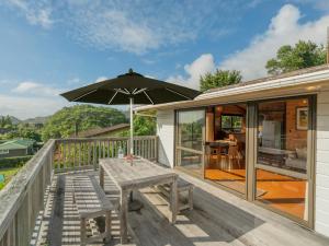 a wooden deck with a table and an umbrella at Beach Lovers Bach - Hahei Holiday Home in Hahei
