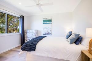 a white bedroom with a large bed with blue pillows at Beachcomber at Currarong - Pet Friendly - 5 Mins Walk to Currarong Rockpools in Currarong