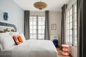 um quarto com uma grande cama branca e janelas em Edgar Suites Louvre - Jour em Paris