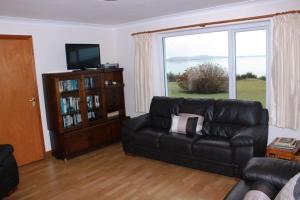 a living room with a black leather couch and a large window at Waterside Cottage, Cashel in Galway