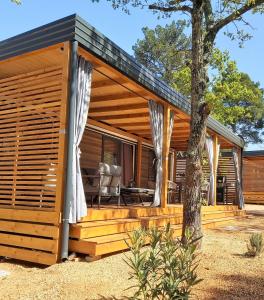 a wooden cabin with a deck with a tree at Mobile Home Sole in Biograd na Moru