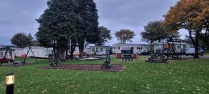 a park with swings and a playground in the grass at 24 The Beeches Caravan Park in Gilcrux